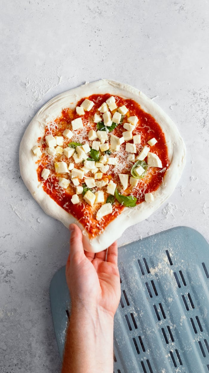 about-02 A hand preparing fresh homemade pizza with cheese and basil. Perfect for gourmet culinary projects.