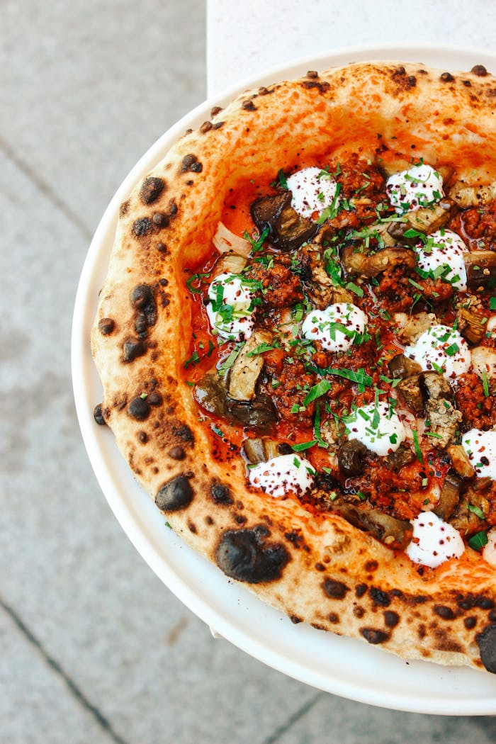 gallery-04 Close-up of a gourmet pizza with cheese, mushrooms, herbs, and tomato sauce.